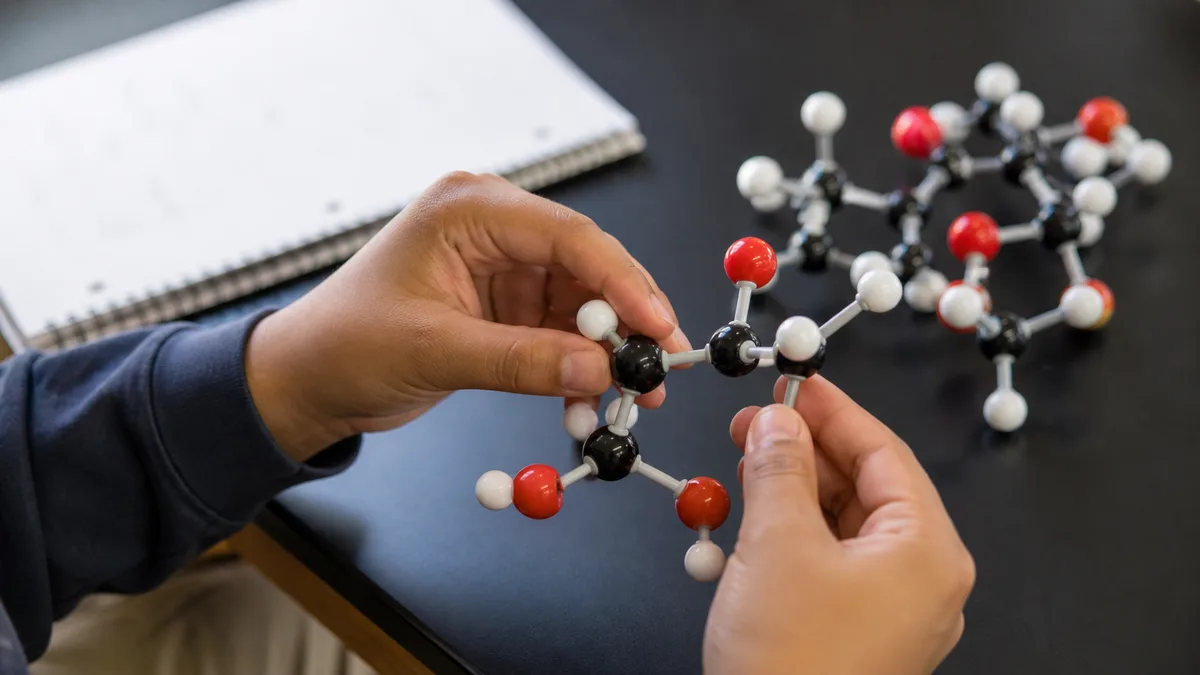 A student's hands rearrange the same colored pieces in a classroom molecular-model kit.