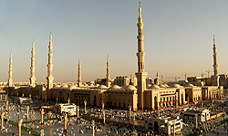Ground-level view of a large mosque complex with multiple minarets, crowded with people in the surrounding plaza